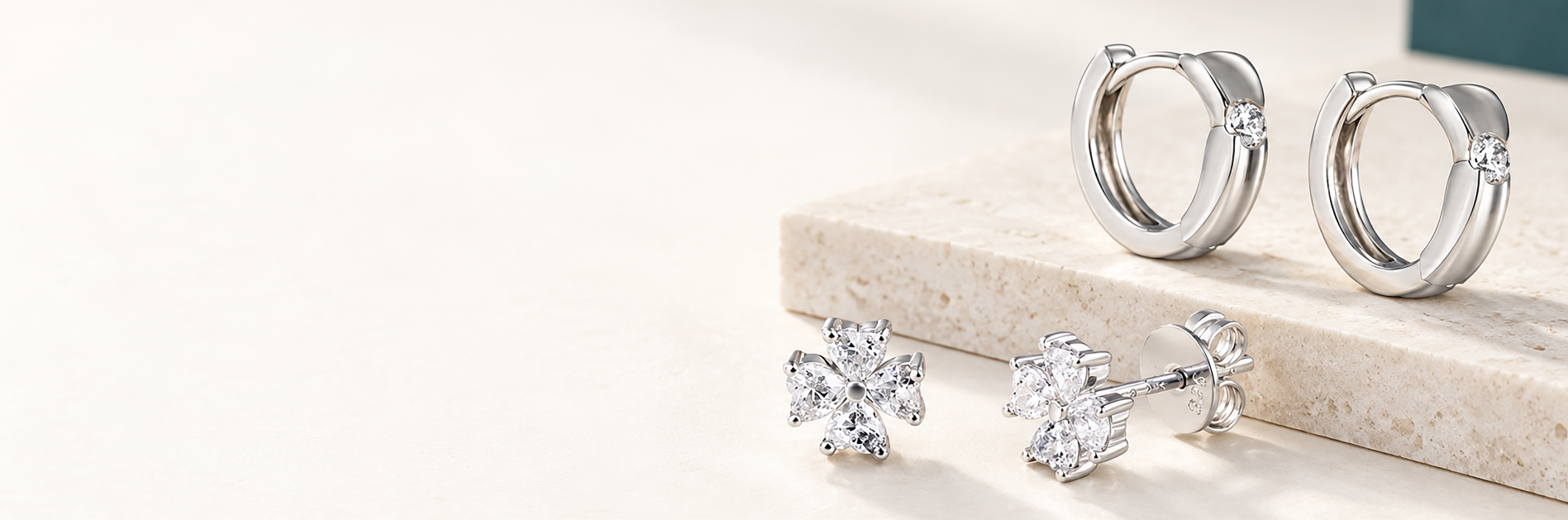 Silver hoop earrings and flower stud earrings arranged on a light stone surface