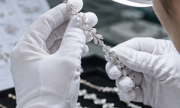 Technician in white gloves inspecting a plated bracelet under a lamp