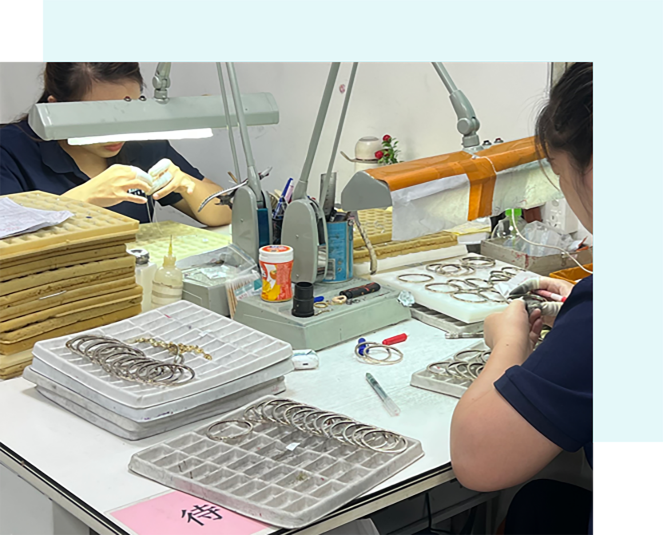 Two jewelers working at a production bench with trays of small batch jewelry components