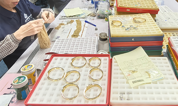 Workers checking gold jewelry components in red trays on a workshop table