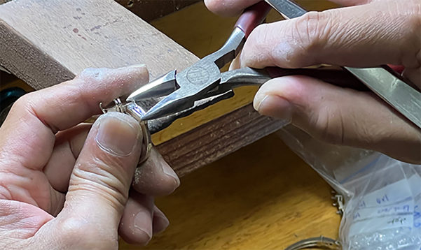 Jeweler trimming a metal ring with cutting pliers at a finishing bench