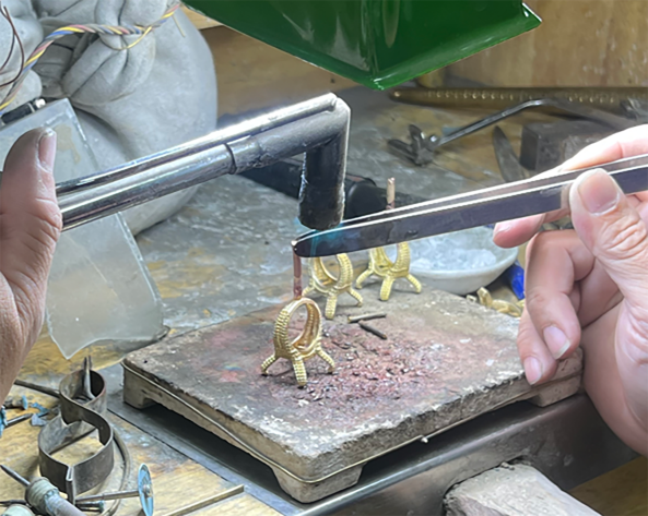 Jeweler cutting a gold ring on a bench pin during finishing and quality checks