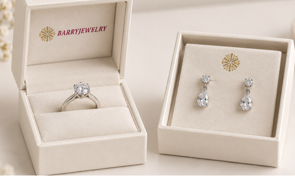 Cream jewelry boxes holding a solitaire ring and a pair of drop earrings in fitted inserts