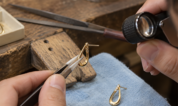 Jeweler cutting and inspecting a gold earring with a saw and loupe at the workbench
