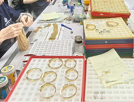 Hands assembling gold jewelry components in a red sorting tray during incoming material inspection