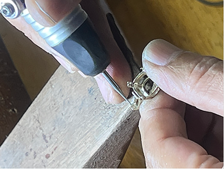 Jeweler inspecting a loose stone with a loupe above a blue work mat before setting