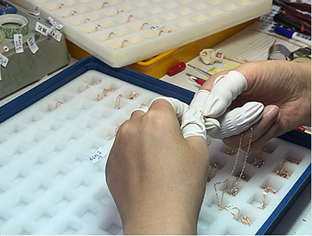 Gloved hands checking small clasps, jump rings and earring backs in a white component tray