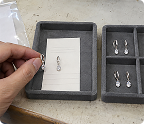 Hand lifting a ring from a grey presentation tray prepared for third party testing